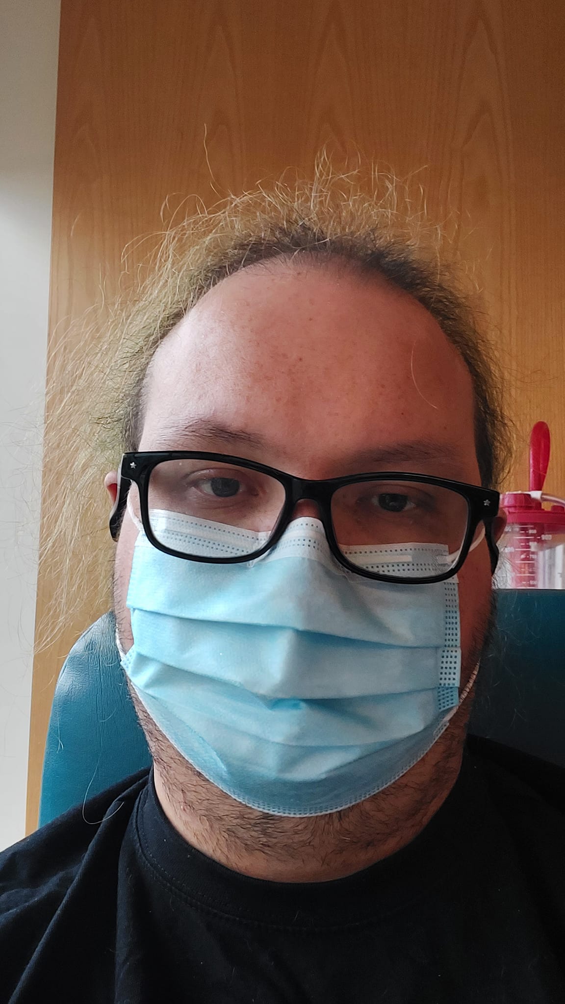 A man wears a surgical mask and sits in the chemo suite, recieving treatment, he looks tired